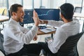 Two men traders sitting at desk at office together monitoring stocks data candle charts on screen analyzing price flow