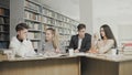 Two men and two women college students laughing while preparing for exams while sitting at table at university library Royalty Free Stock Photo