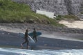 Two men walking on a black beach to surf