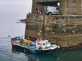 Two men with a white van lift a plastic container of fish from the desk of a small fishing boat at low tide in Craster Harbour, Royalty Free Stock Photo