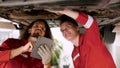 two men who are mechanics, working in large garage, two mechanics checking undercarriage car raised high see lower part clearly, Royalty Free Stock Photo