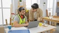 Two men in a woodworking workshop collaboratively studying a laptop on a workbench Royalty Free Stock Photo