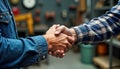 Two men in work clothes exchange handshake in industrial workshop. Close-up image highlights teamwork, cooperation. Professional Royalty Free Stock Photo