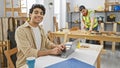 Two men working in a bright carpentry workshop, one programming on a laptop and another measuring wood Royalty Free Stock Photo