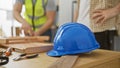Two men working together in a carpentry workshop with tools and a blue hardhat on a wooden table Royalty Free Stock Photo