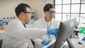 Two men working together in a laboratory, analyzing data on a computer screen amid scientific equipment Royalty Free Stock Photo