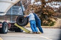 Two men working together to load a duel tired from a long-haul trailer using a wooden ramp - selective focus