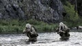 Two mercenary soldiers ford a river during a special operation.