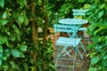 Two metal courtyard and patio chairs and table in serene, peaceful, lush, private backyard at home on a summers day Royalty Free Stock Photo