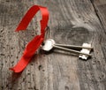 Two metal house door keys with red ribbon on a woodenbackground