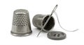 Two metallic thimbles, one upright and one on its side, rest beside a threaded needle Royalty Free Stock Photo