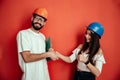 Two mid adults constructors workers giving hand shake isolated on red background