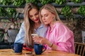 Two mid age women friends sitting in cafe looking at mobile phone and drinking coffee. Smiling girls chatting indoors Royalty Free Stock Photo