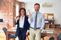 Two middle age business workers standing working together in a meeting at the office doing happy thumbs up gesture with hand Royalty Free Stock Photo