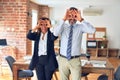 Two middle age business workers standing working together in a meeting at the office doing ok gesture like binoculars sticking Royalty Free Stock Photo