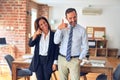 Two middle age business workers standing working together in a meeting at the office smiling doing phone gesture with hand and Royalty Free Stock Photo