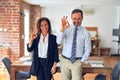 Two middle age business workers standing working together in a meeting at the office smiling positive doing ok sign with hand and Royalty Free Stock Photo