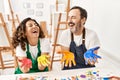 Two middle age student smiling happy showing paint hands at art studio
