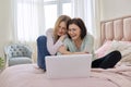 Two middle aged women having rest sitting together at home on bed, looking in laptop screen. Royalty Free Stock Photo