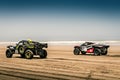 Two mighty rally raid buggies racing over the beach next to the sea. Start of the Morocco Desert Challenge 2023
