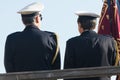 Two military old of men in suits stand next to the flag of Venice