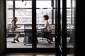 Two millennial businesswomen meeting for a job interview, full length, seen through glass wall