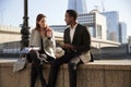 Two millennial colleagues take a break sitting on the embankment eating near London Bridge by the River Thames, close up Royalty Free Stock Photo