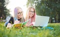 Two millennial university student girls lying in the grass in campus - Young smiling friends using laptop and writing in booklet Royalty Free Stock Photo