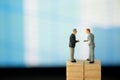 Two miniature businessmen shaking hands and standing on wooden blocks Royalty Free Stock Photo