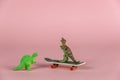 Two miniature dinosaurs and a mini skateboard against the pink background. Small green miniatures of predatory dinosaurs. Close-up