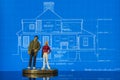 Two miniature figures standing on a house blueprint as if discussing the plans macro Royalty Free Stock Photo