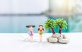 Two miniature girl in swimwear with coconut tree over blurred swimming pool background