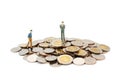 Two miniature people walking and standing on pile of new Thai Baht coins, isolated on white background. Royalty Free Stock Photo