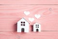 Two miniature white toy houses with hearts on pink wooden background