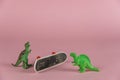 Two miniatures of dinosaurs and an upside-down mini skate against a pink background. Small green miniatures of predatory dinosaurs Royalty Free Stock Photo