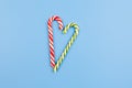 Two Mint hard candy canes striped in Christmas colours on blue background. Closeup. Heart sign