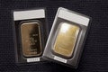 Two minted gold bars against a dark fabric texture