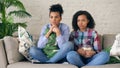 Two mixed race curly girl friends sitting on the couch and watch thriller movie and eat popcorn at home Royalty Free Stock Photo