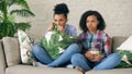 Two mixed race curly girl friends sitting on the couch and watch very scary movie on TV and eat popcorn at home Royalty Free Stock Photo