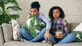 Two mixed race curly girl friends sitting on the couch and watch very scary movie on TV and eat popcorn at home Royalty Free Stock Photo