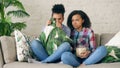 Two mixed race curly girl friends sitting on the couch and watch very scary movie on TV and eat popcorn at home Royalty Free Stock Photo