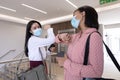 Two businesswomen wearing face masks greeting each other by touching elbows at modern office