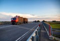 Two modern logging trucks transport round logs along the highway in the summer evening. Logging as a business, wood