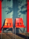 Two modern orange plastic chairs against a blue corrugate wall.