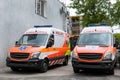 Two modern white and orange ambulance medical emergency vans truck parked near hospital building. Paramedic vehicles on