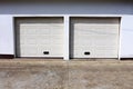 Two modern white rollup garage doors with cracked concrete driveway mounted on white wall