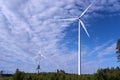 Two modern white windmills stand high above green forest, sunny summer day. Sweden, green energy Royalty Free Stock Photo