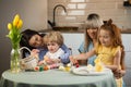 Two mothers with their children coloring Easter eggs while sitting in the kitchen. Royalty Free Stock Photo