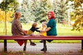 Two mothers and their daughters are sitting on a park bench. Women and children in nature in autumn