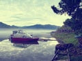 Two red and white motor boats moored to the shore of a mountain lake with calm water in an early foggy morning Royalty Free Stock Photo